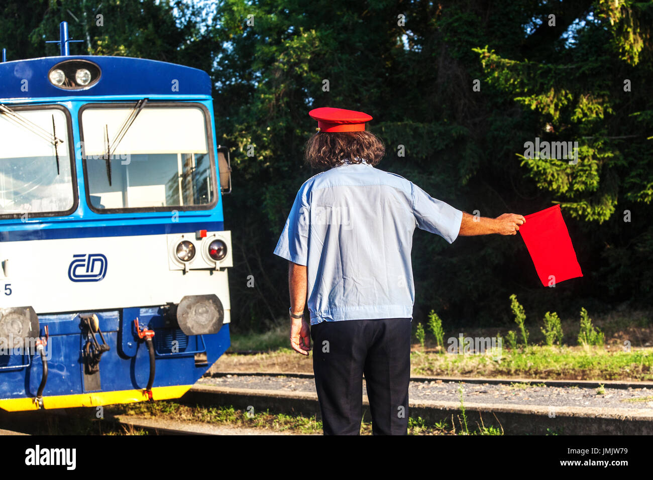 Treno ceco in campagna Un uomo che segnala con un cappello rosso un treno con una bandiera rossa, ferrovia Ceca, treno Repubblica Ceca Ceske Drahy Company CD Foto Stock