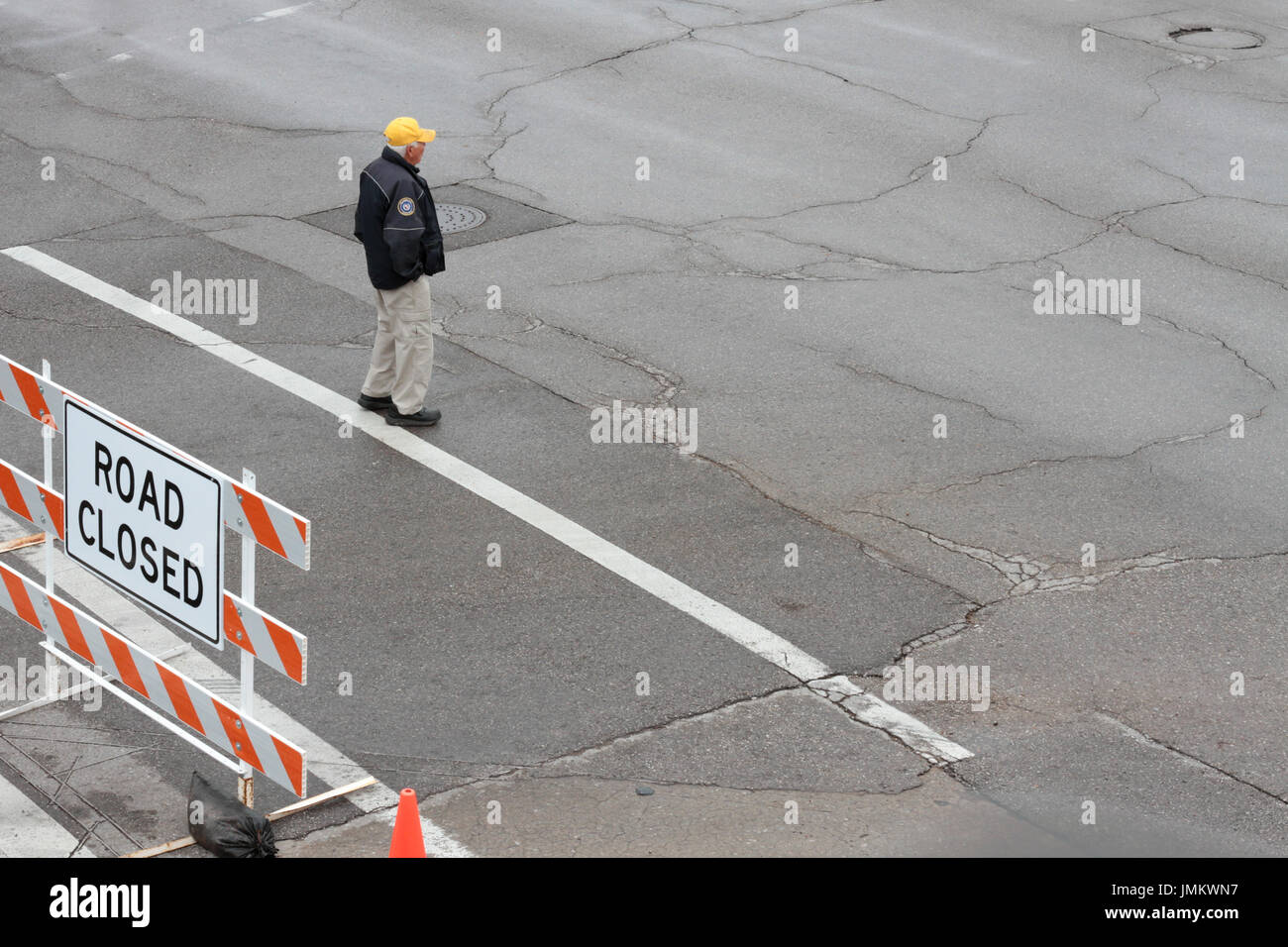 Un lavoratore della città sorge in un vuoto di strada bagnata accanto a una strada chiusa segno. Foto Stock