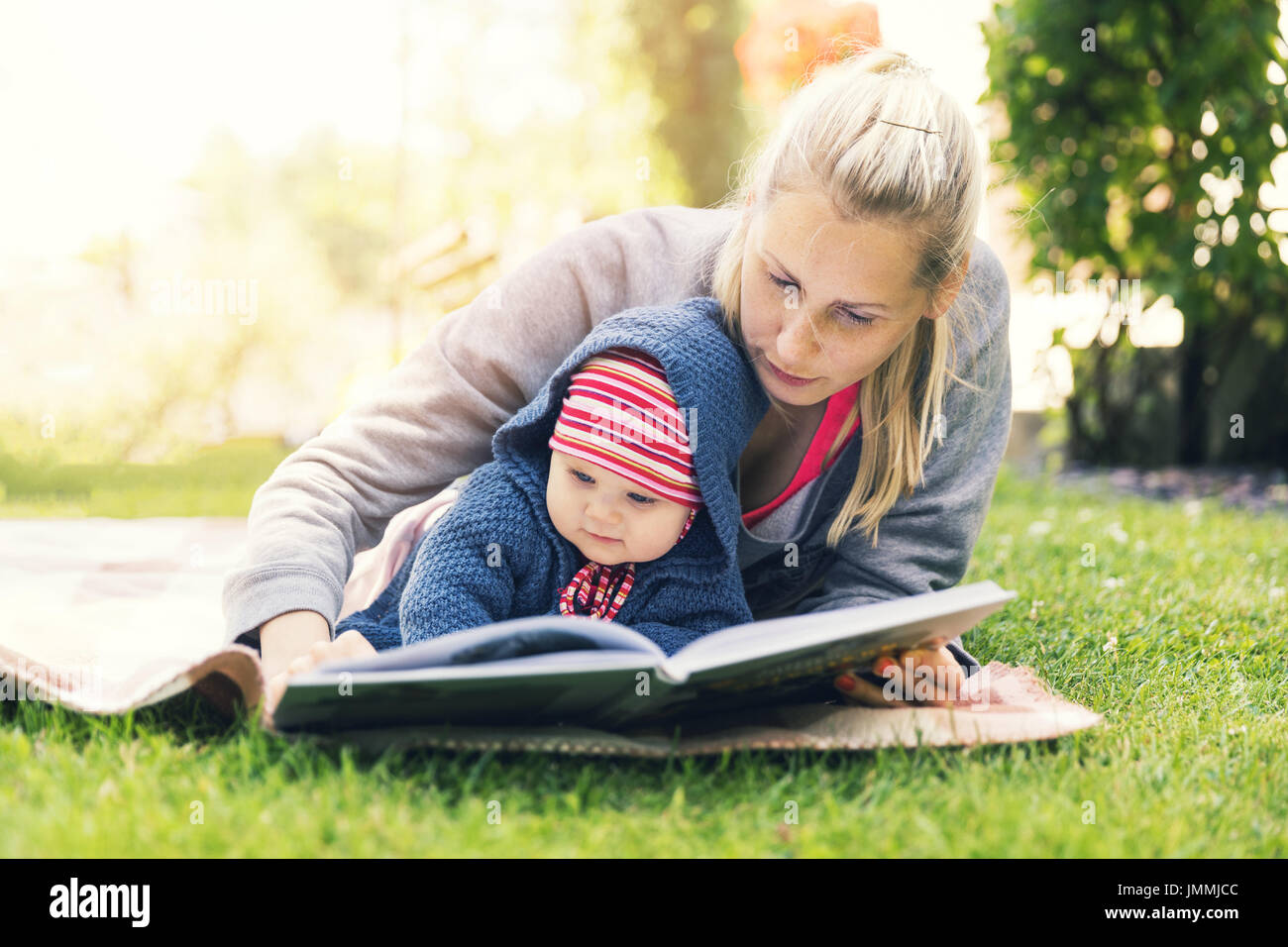 Madre la lettura di un libro per baby in giardino nel cortile su una coperta Foto Stock
