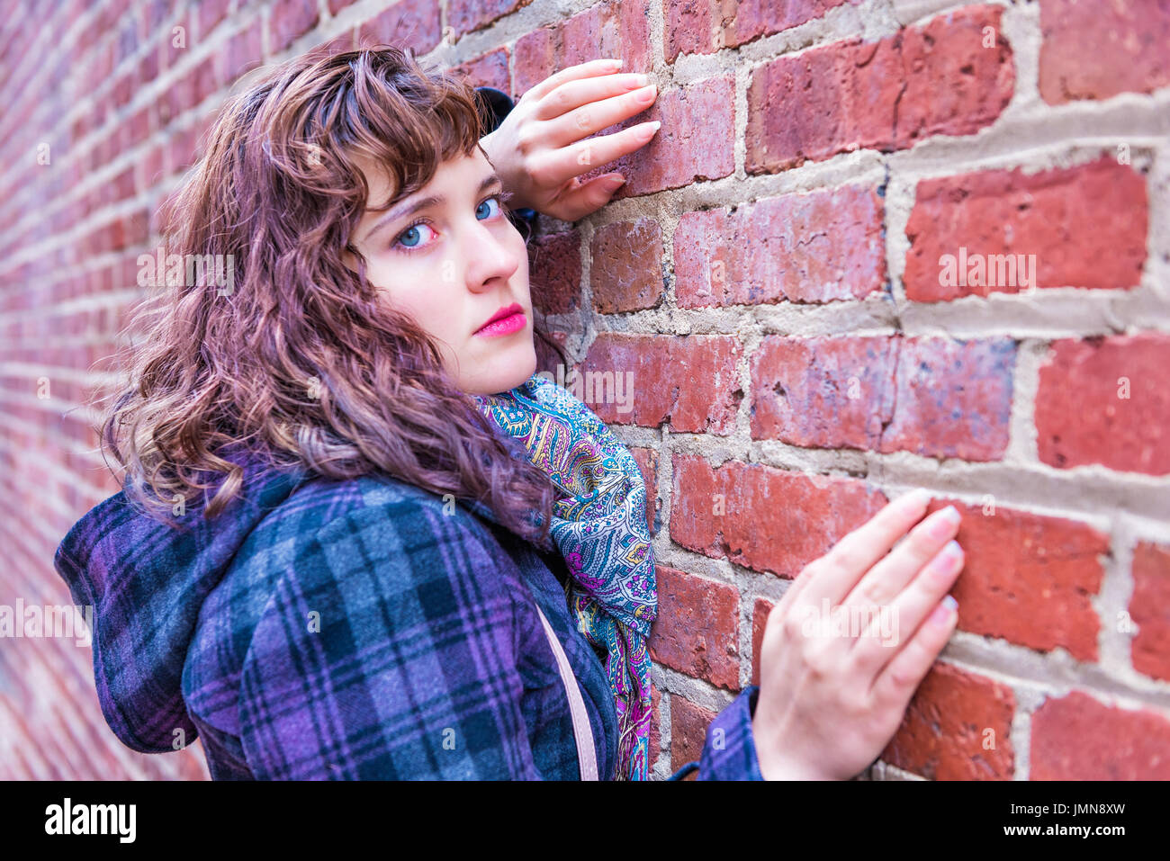 Giovane donna appoggiata contro un muro di mattoni nel rivestire durante il periodo invernale Foto Stock