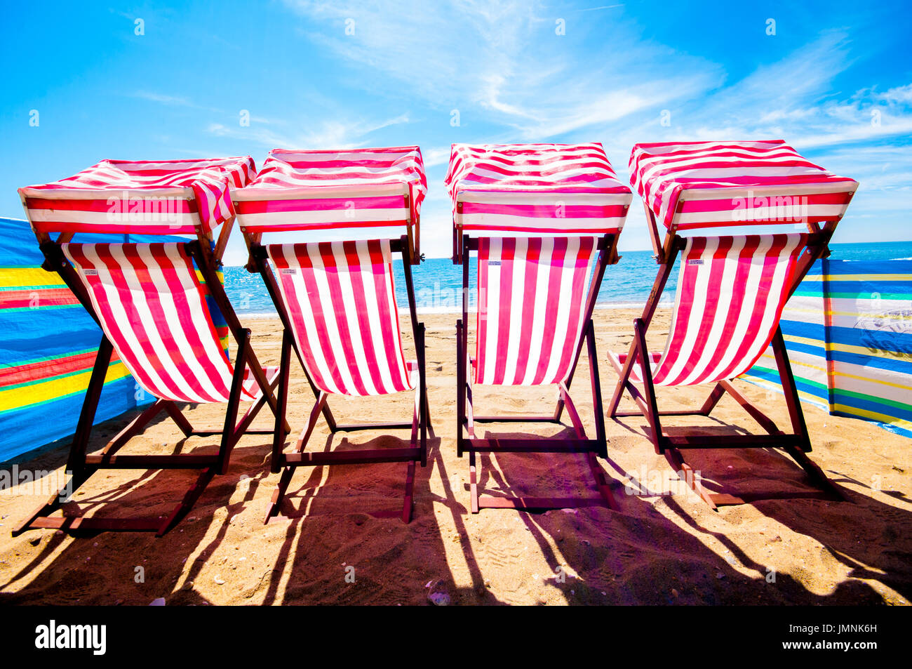 Quattro sedie a sdraio sulla spiaggia di sabbia al giorno d'estate e di sole blu cielo Foto Stock