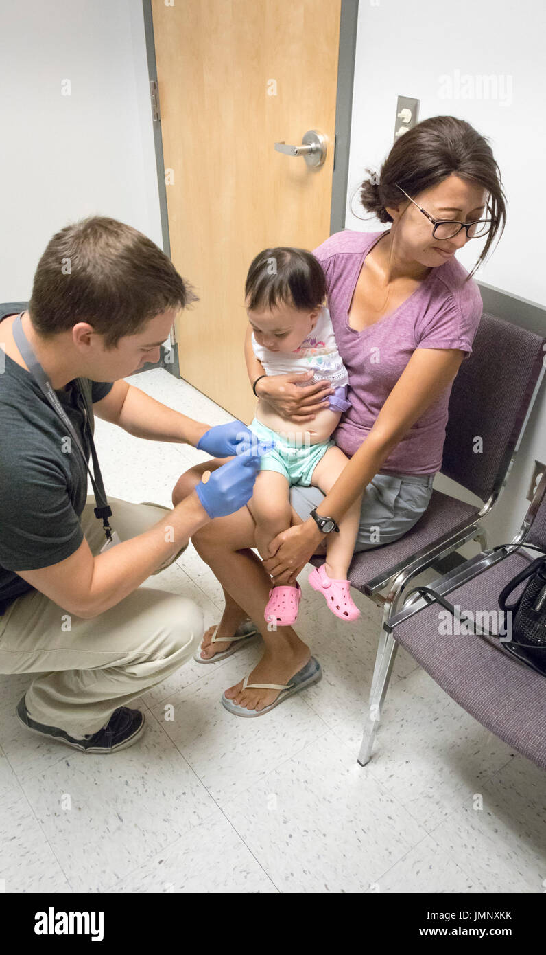 Baby tenuto da ansiosa madre riceve la vaccinazione di iniezione nell'ufficio del medico Foto Stock