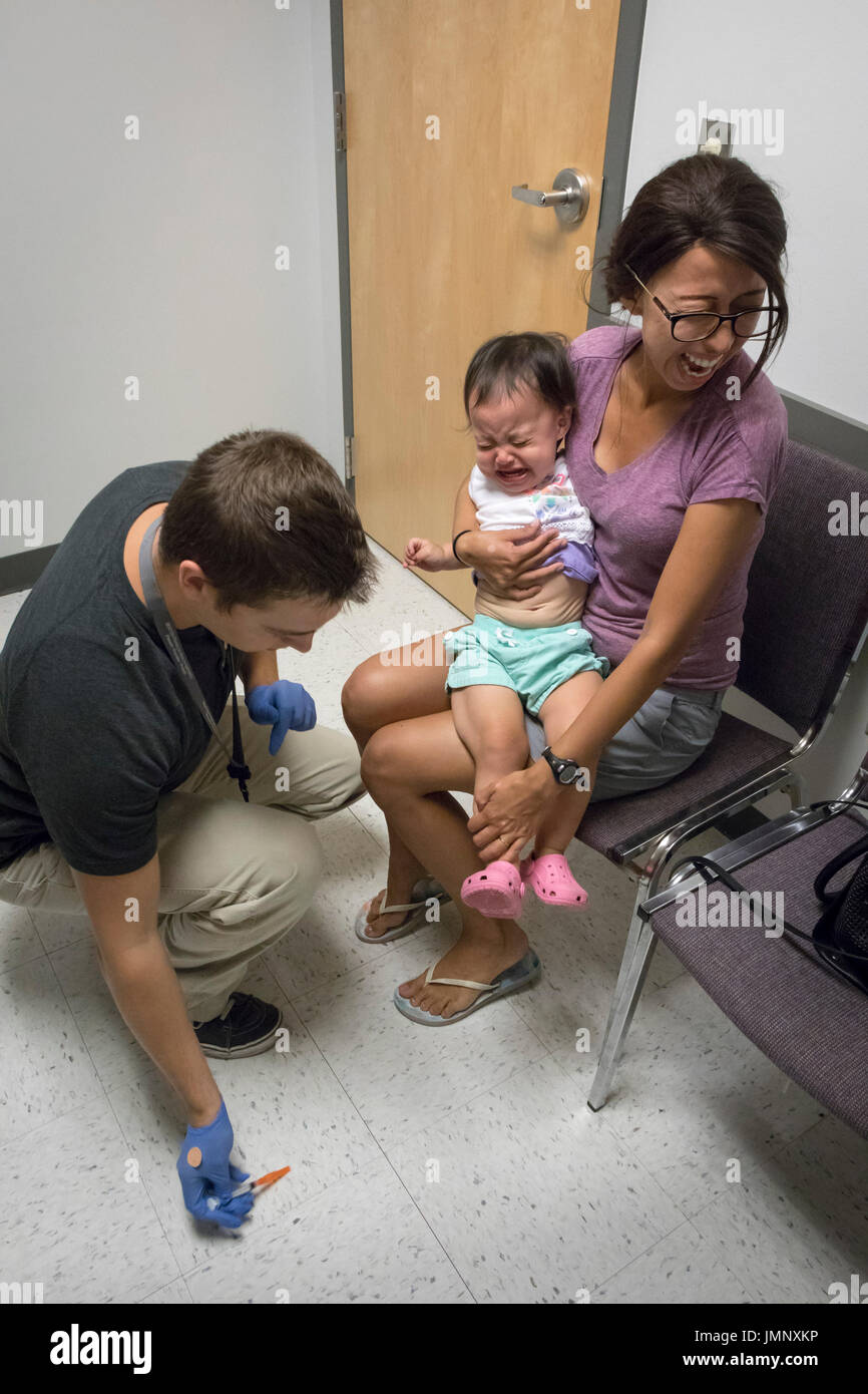 Baby tenuto da ansiosa madre riceve la vaccinazione di iniezione nell'ufficio del medico Foto Stock