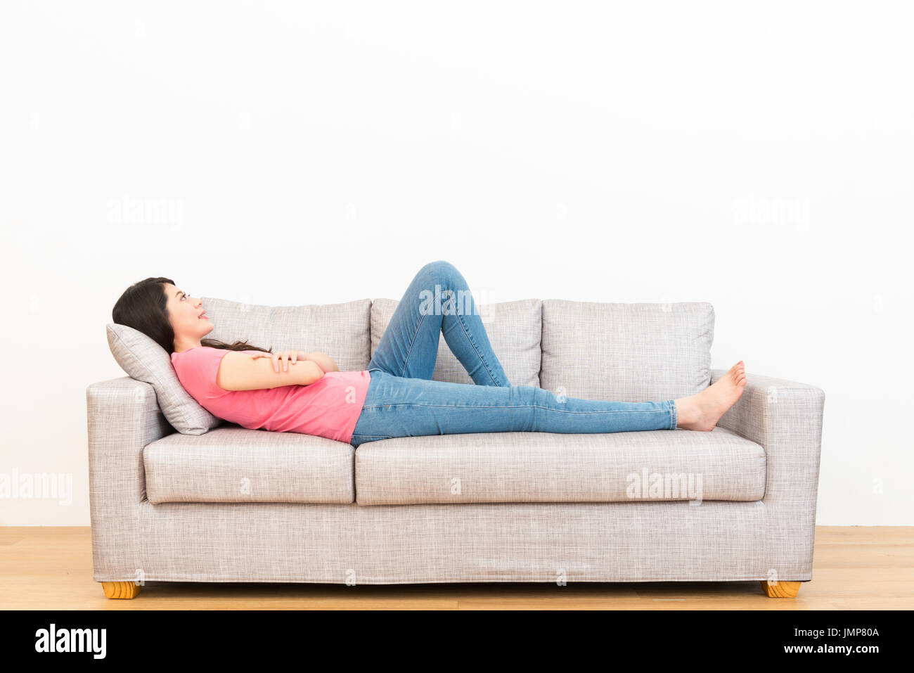 Donna sorridente sdraiato sul lettino divano guardando lo sfondo bianco piacevole giornata del pensiero sognando su pavimento di legno godendo le vacanze a casa. Foto Stock