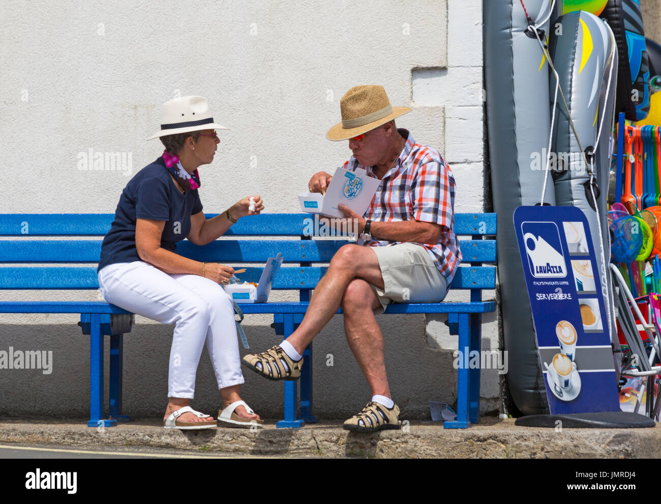 Coppia seduta sul banco di mangiare pesce e patatine a Lyme Regis, Dorset in luglio Foto Stock