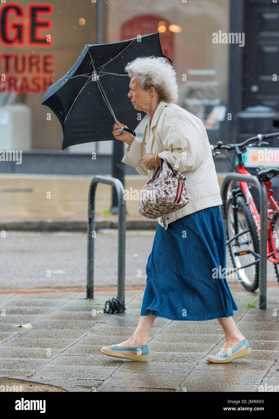 Signora anziana donna sotto la pioggia e il vento tenendo un ombrello. Foto Stock