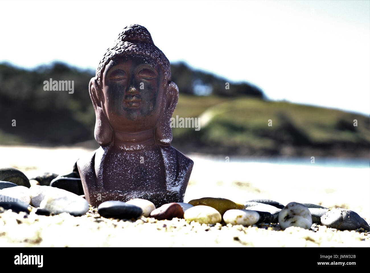 Meditando la statua di Buddha sulla sabbia in ambiente esterno. In ambiente naturale statua di Buddha a spiaggia con ciottoli e pietre onde del mare e il blu del cielo Foto Stock