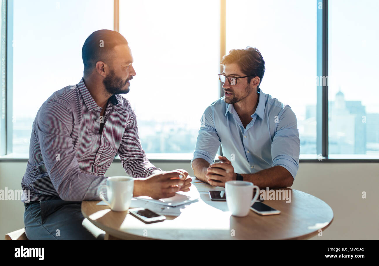 dirigenti aziendali che discutono del lavoro in ufficio. Due uomini d'affari seduti su un tavolo rotondo e a discutere di affari. Foto Stock