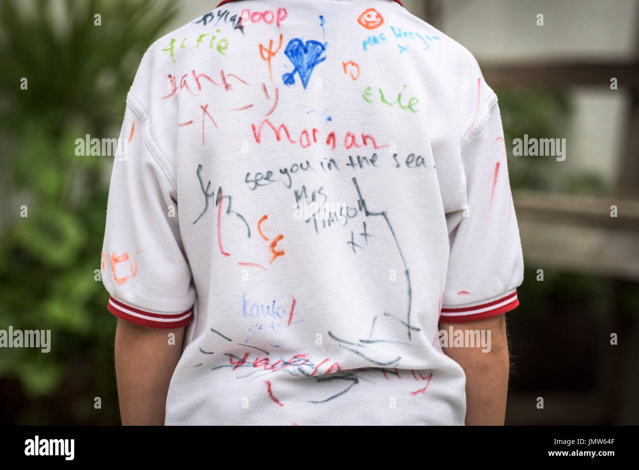 Un giovane Junior scolaro che indossa una camicia bianca firmata da tutti i suoi amici alla fine della scuola estate termine. Newquay, Cornwall. Foto Stock