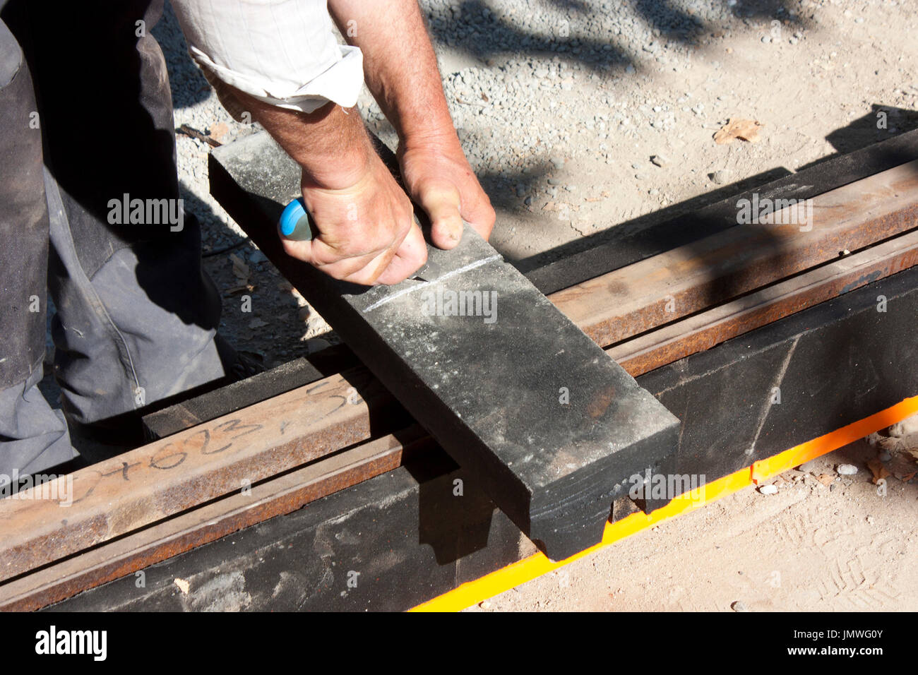 Uomo al lavoro su light rail sito in costruzione, il taglio di materiale smorzatore di vibrazioni per tram binari di riduzione del rumore Foto Stock