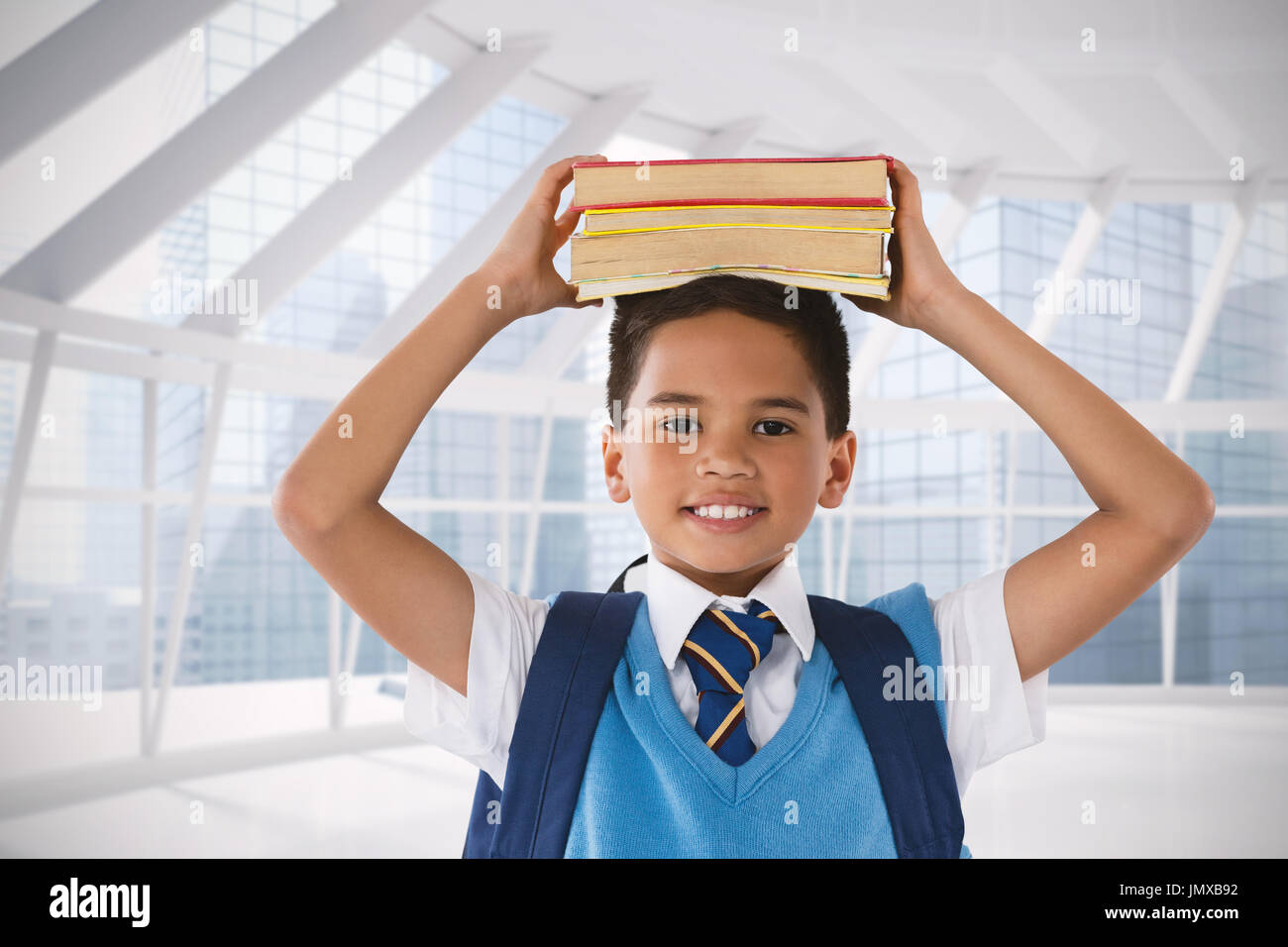 Sorridente schoolboy trasporto di libri sulla testa su sfondo bianco contro le moderne camera con vista città Foto Stock