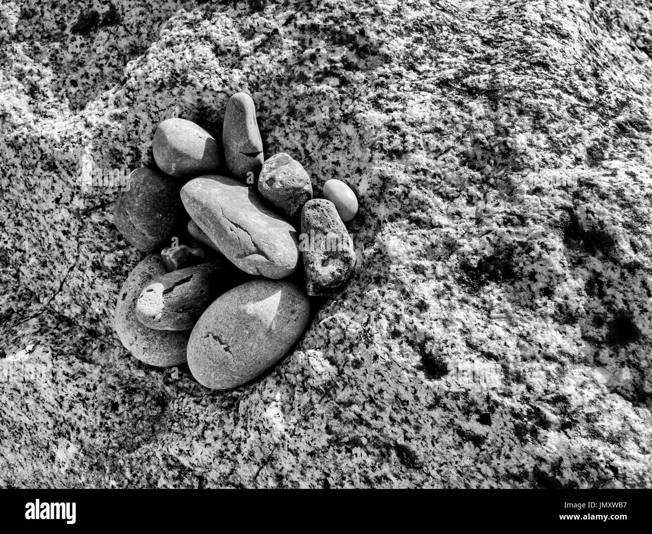 Usurato e ciottoli tondi formare modelli interessanti nelle intercapedini tra le rocce di una roccia corazza groyne su una spiaggia di Devon. Foto Stock