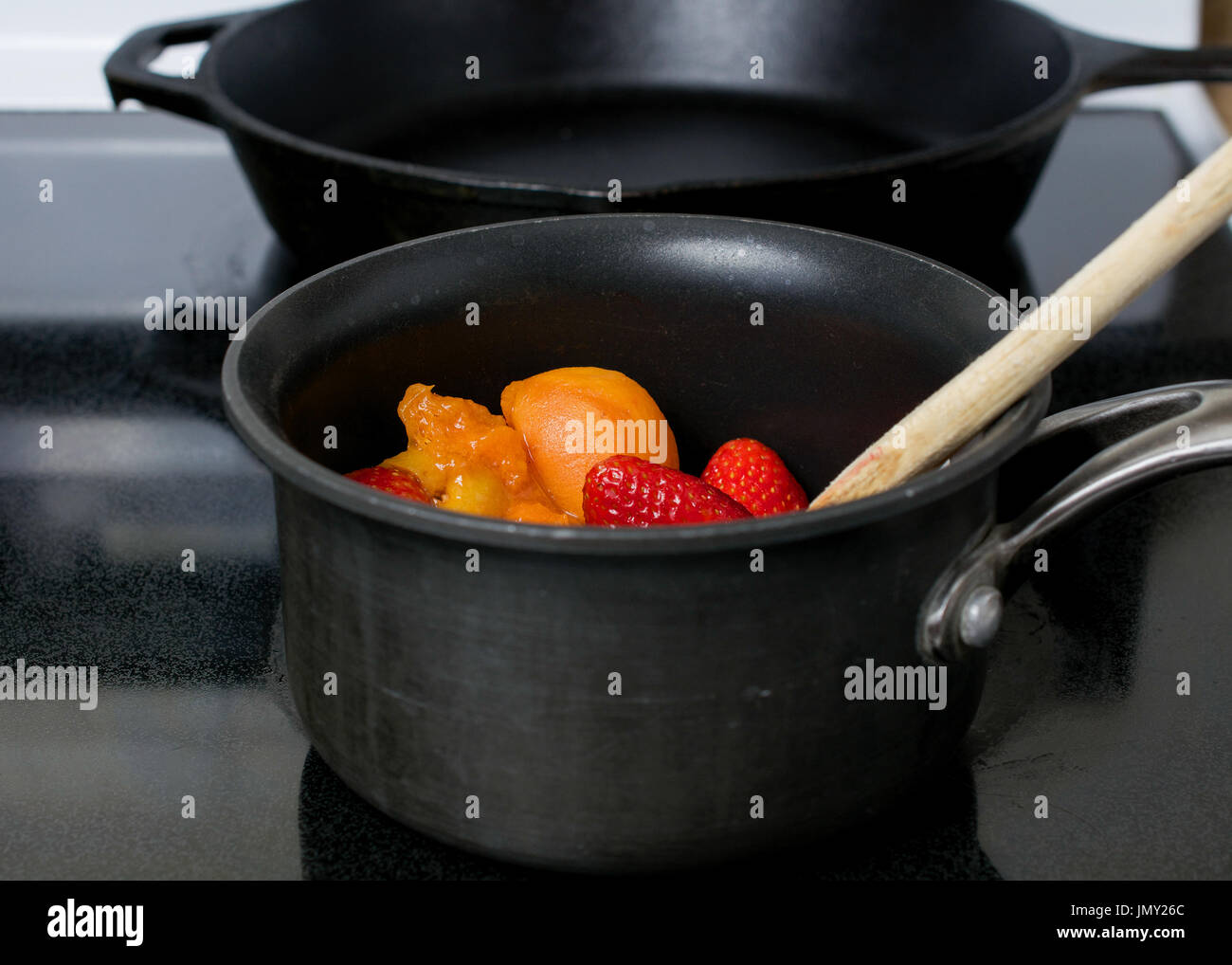 Realizzazione di albicocca e gelatina di fragola in una padella antiaderente sulla parte superiore di una stufa elettrica Foto Stock