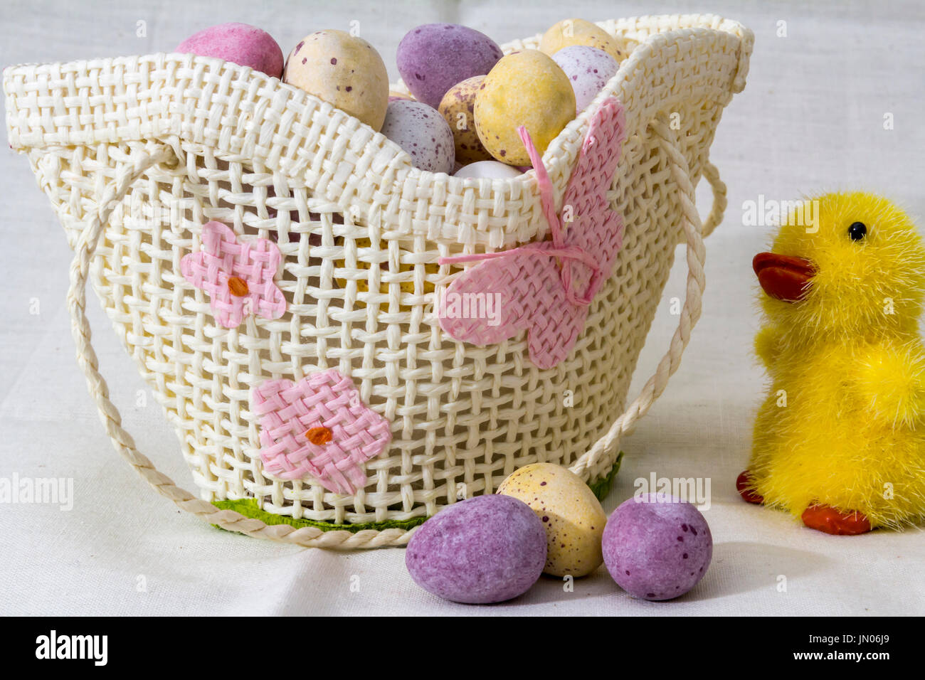 Mini uova di cioccolato in un piccolo cestino di vimini giocattolo con un pulcino giocattolo a lato e tre uova nella parte anteriore del cestello. Foto Stock