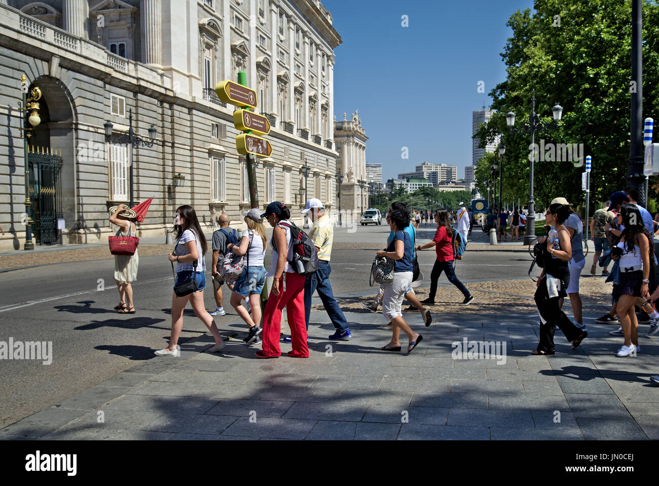 Gruppo turistico di attraversare una strada vicino a al Palazzo Reale di Madrid. Tour guida porta il gruppo tenendo un ombrello rosso. Foto Stock