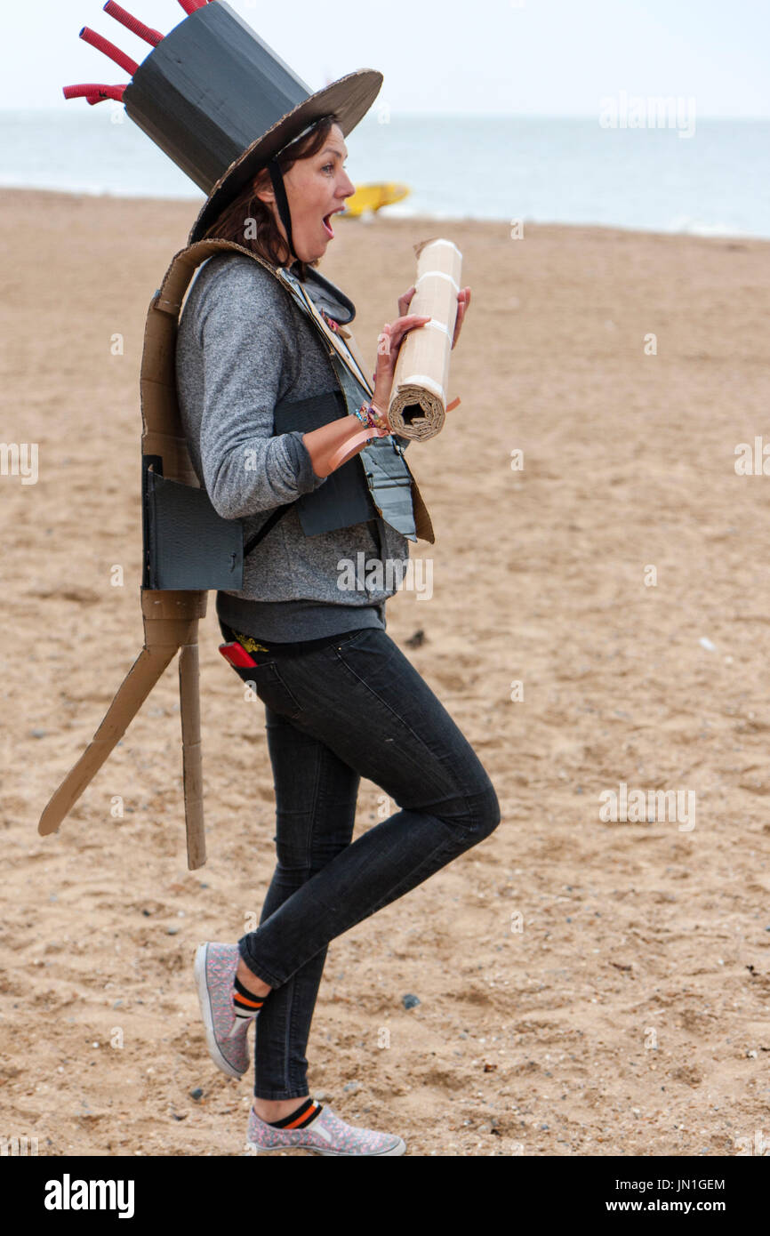 Cardboardia evento su Ramsgate Beach. Donna, 30s, nella stufa black hat, tenendo lungo palo di cartone. Vista laterale, pone in piedi su una gamba sola guardando in avanti. Espressione facciale di sorpresa. Foto Stock