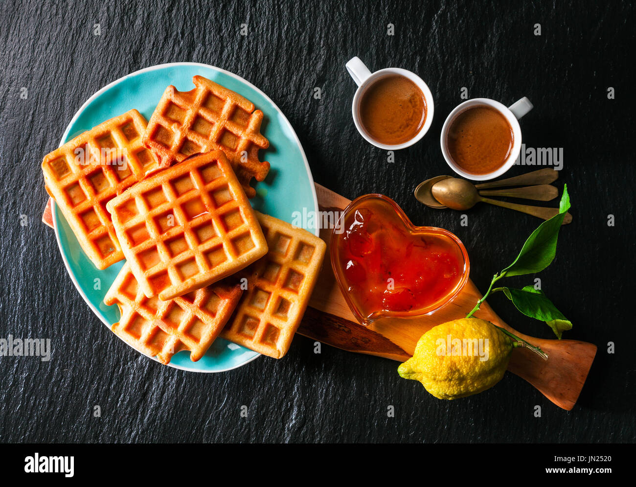 La prima colazione con cialde belghe, confettura di albicocca e caffè su una pietra nera sullo sfondo Foto Stock