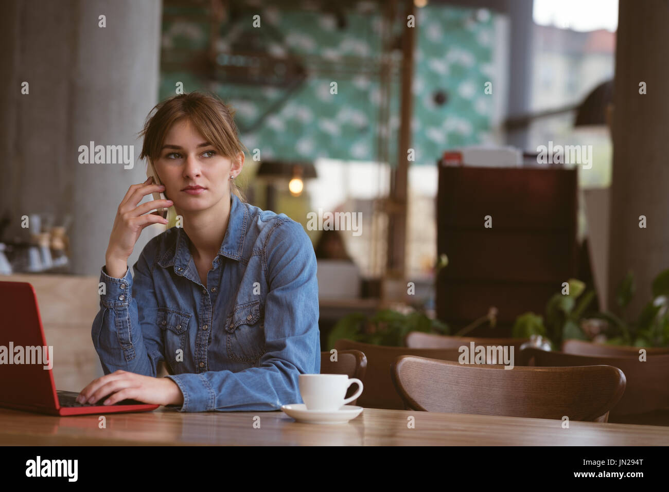 Bella donna parlando al telefono cellulare durante l'utilizzo di laptop in cafe Foto Stock