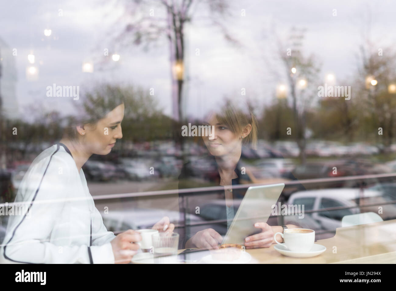 Donna sorridente amici discussioni su tavoletta digitale mentre è seduto in cafe visto attraverso la finestra Foto Stock
