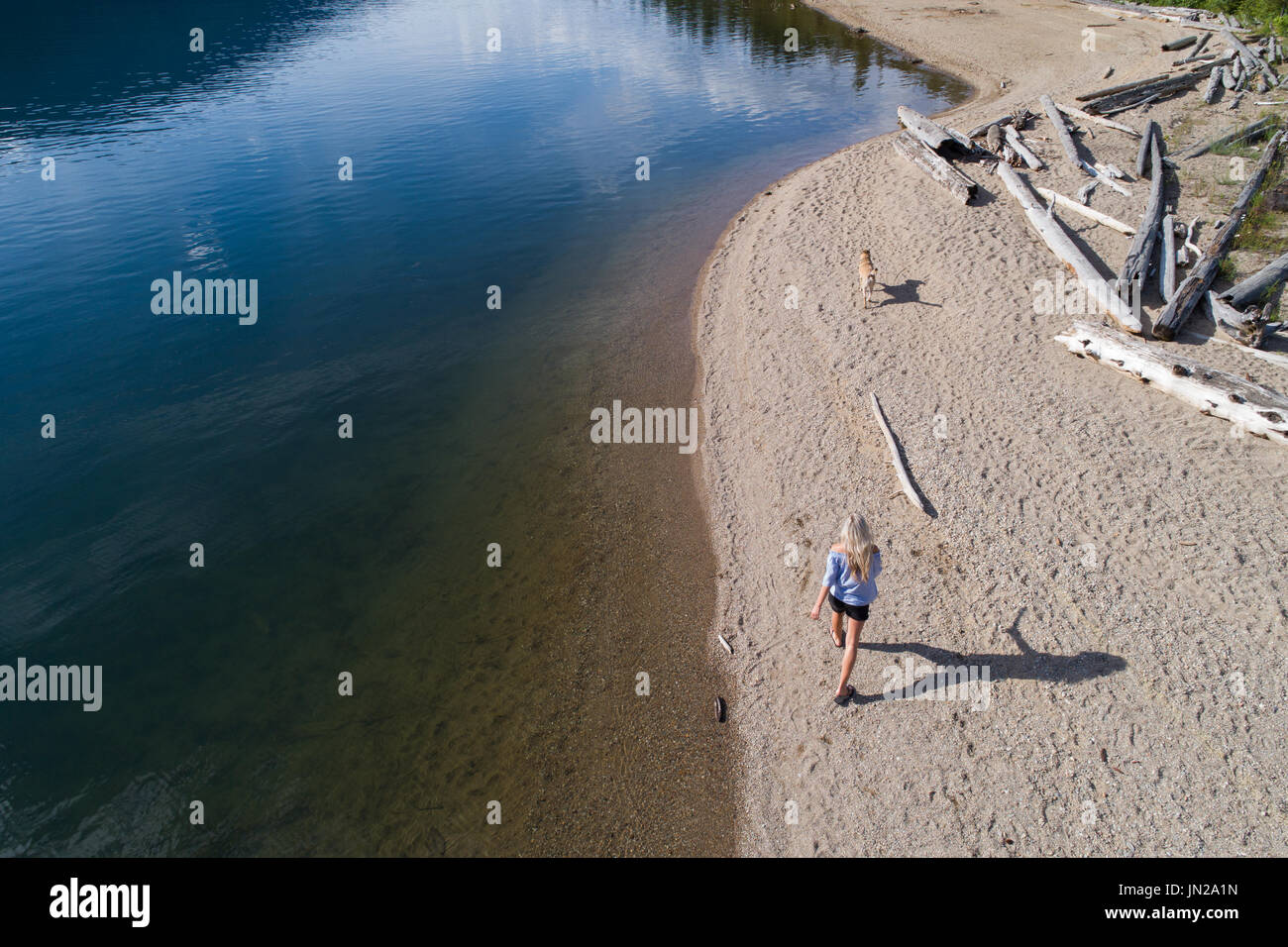 Donna che cammina con il cane sulla riva del lago in una giornata di sole Foto Stock