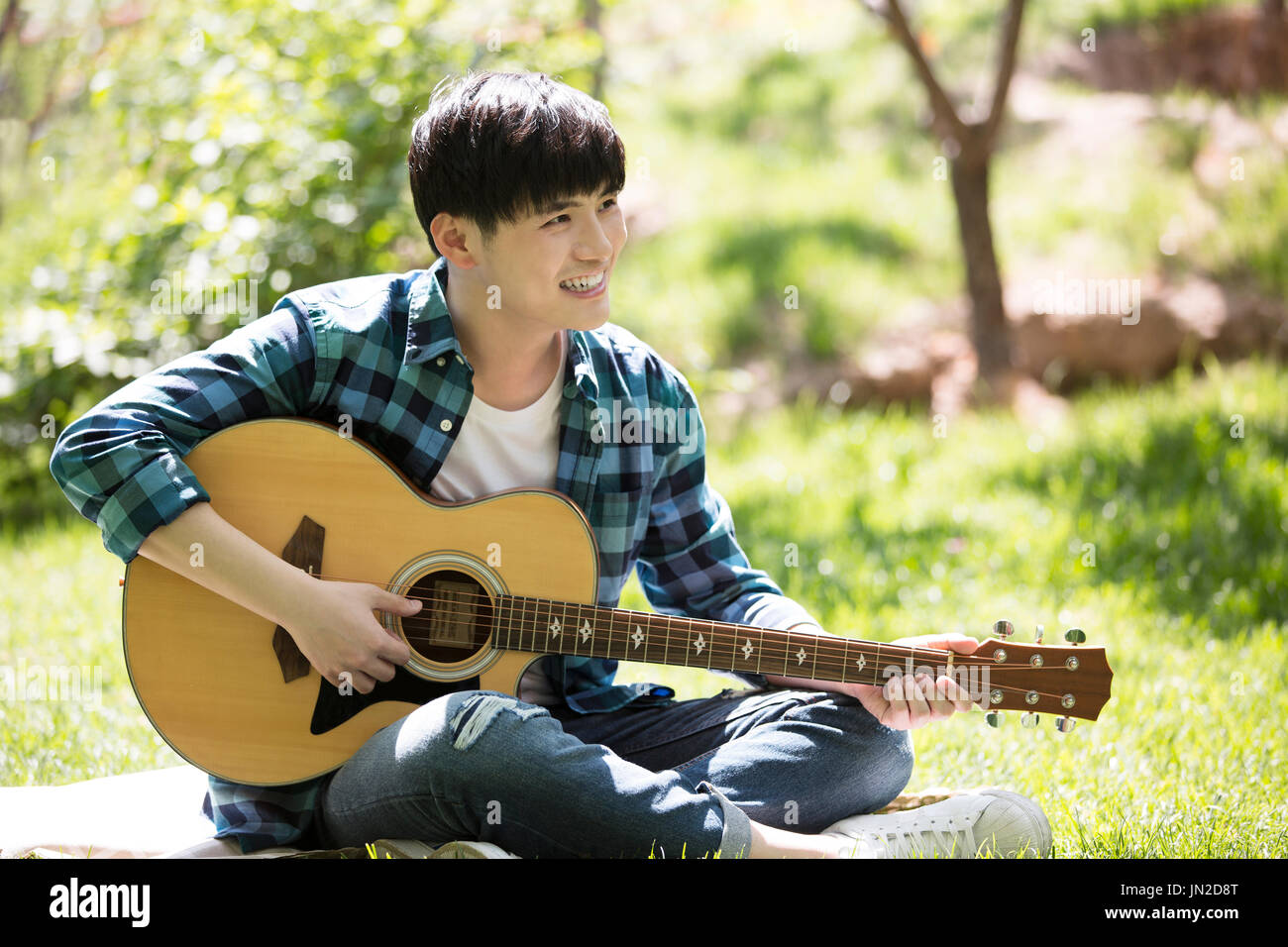 Giovane uomo suonare la chitarra sull'erba Foto Stock