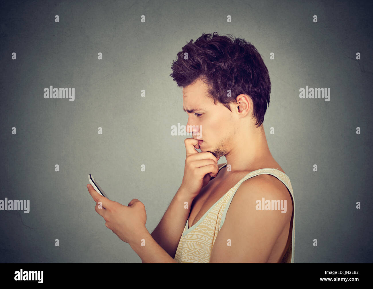 Profilo laterale uomo cercando confuso al suo telefono cellulare isolato su sfondo grigio Foto Stock