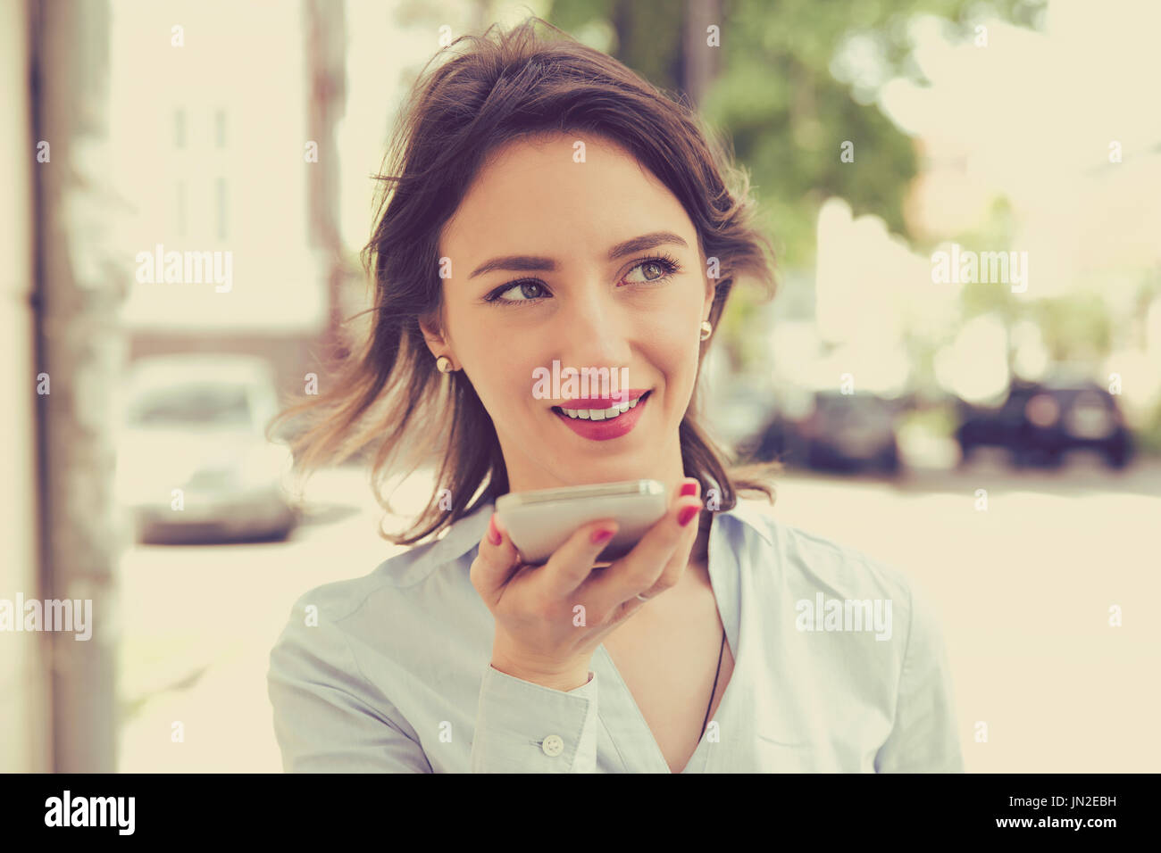 Donna che utilizza un telefono intelligente funzione riconoscimento vocale online a camminare su una strada di città in un giorno di estate Foto Stock