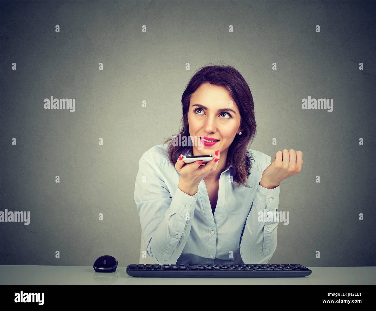 Donna che utilizza un telefono intelligente funzione riconoscimento vocale sulla linea seduta a tavola isolato sul muro grigio sfondo Foto Stock
