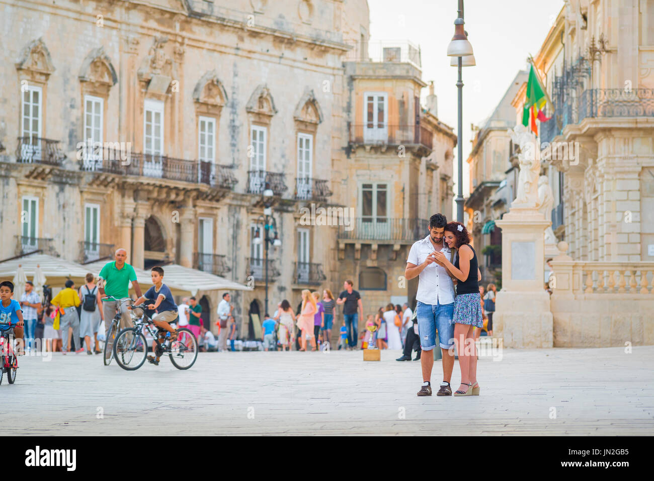 Coppia guardando telefono Europa, vista di una giovane coppia turistica guardare un telefono mentre si trova in una piazza in una città mediterranea. Foto Stock