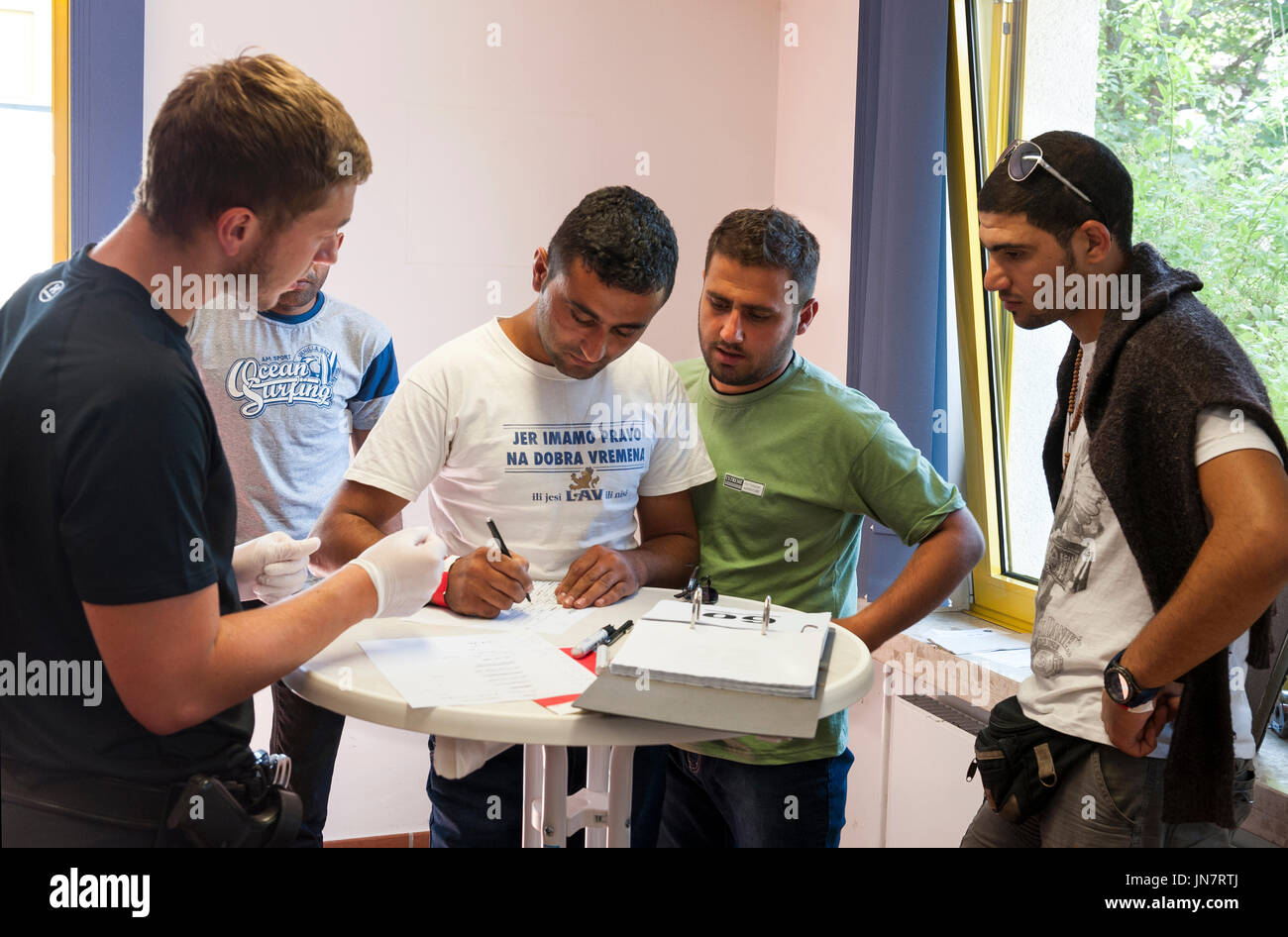 Passau, Germania - August 1th, 2015: un funzionario di polizia richiede la firma di un uomo alla sua registrazione presso il centro di registrazione per i migranti Foto Stock