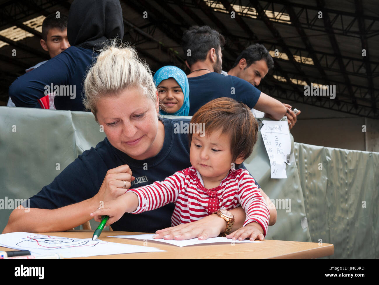 Passau, Germania - 1 Agosto 2015: in Germania un funzionario di polizia si prende cura di un piccolo bambino di rifugiati nell'area di registrazione di Passau. Foto Stock