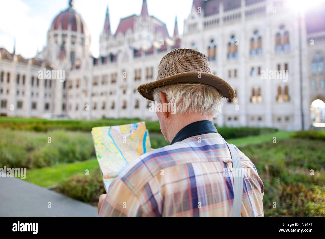 Senior uomo turistica in hat ricerca per la destinazione sulla mappa al parlamento ungherese, Budapest, Ungheria Foto Stock