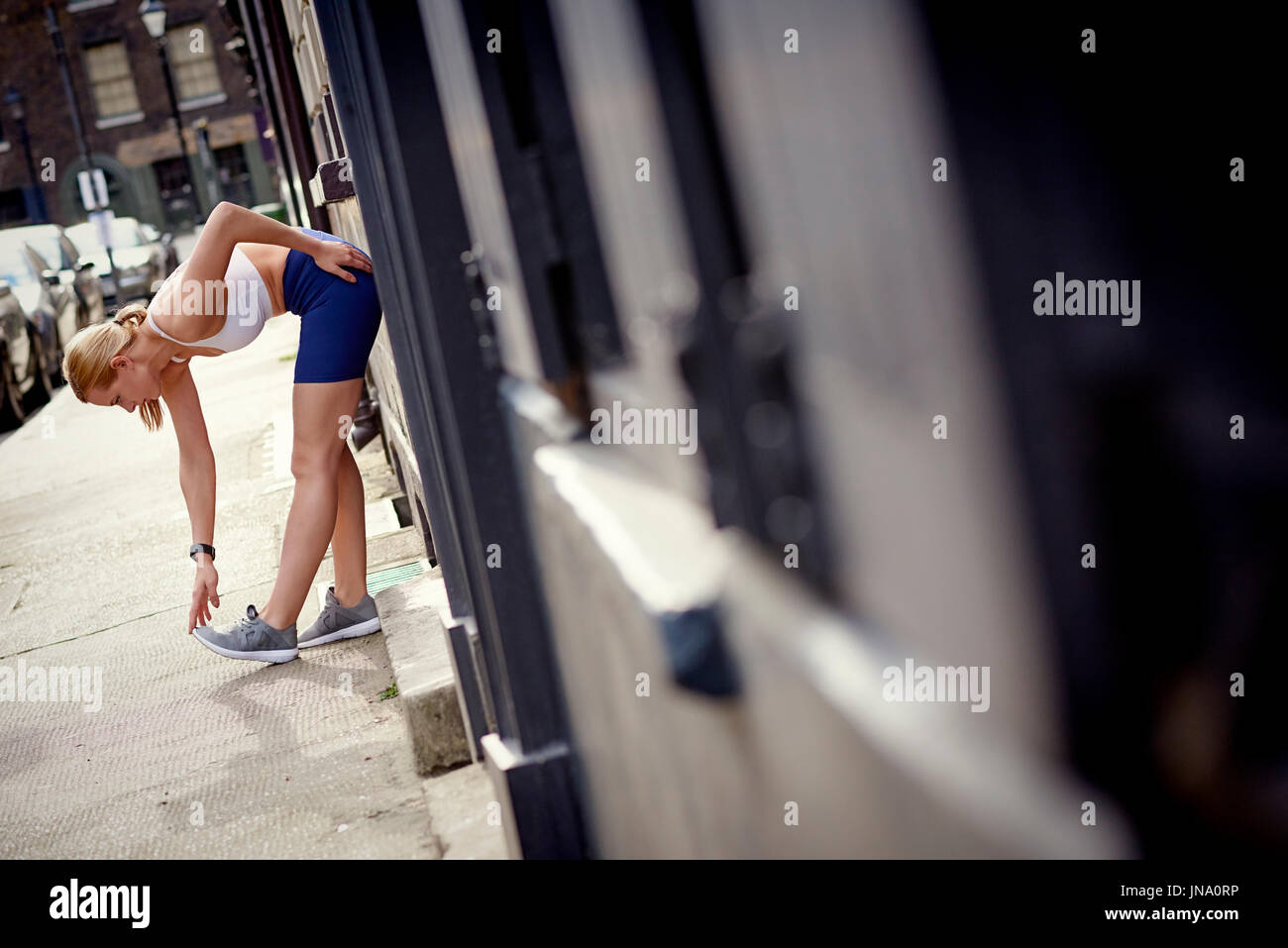 Donna fuori per una corsa in appoggio e stretching in ambiente urbano. Foto Stock