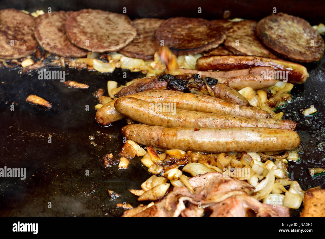 Salsicce, hamburger, pancetta e cipolle cottura su piastra Foto Stock