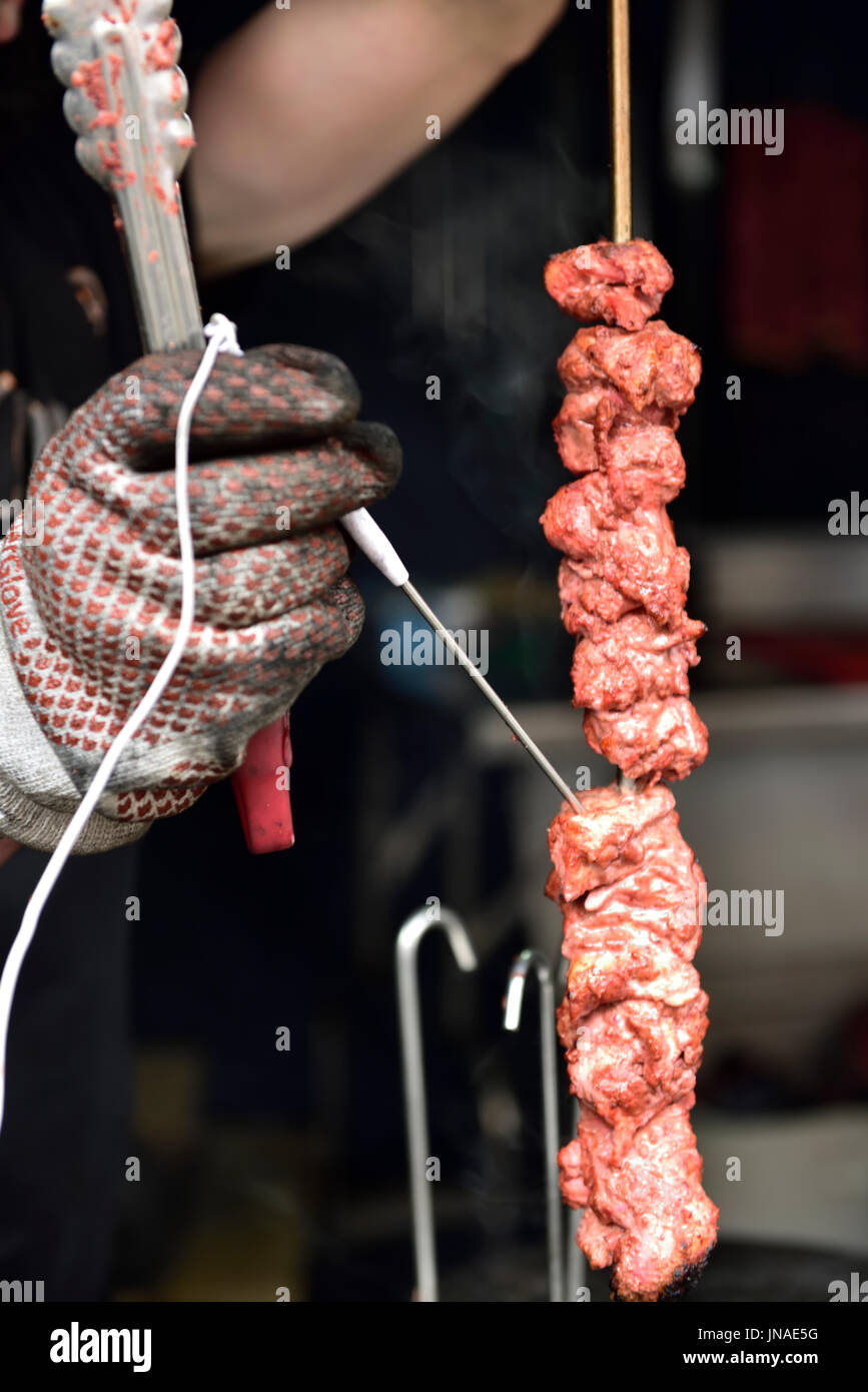 Tenendo la lettura della temperatura con termometro elettronico di kebab su spiedino per verificare la presenza di una cucina sicura Foto Stock