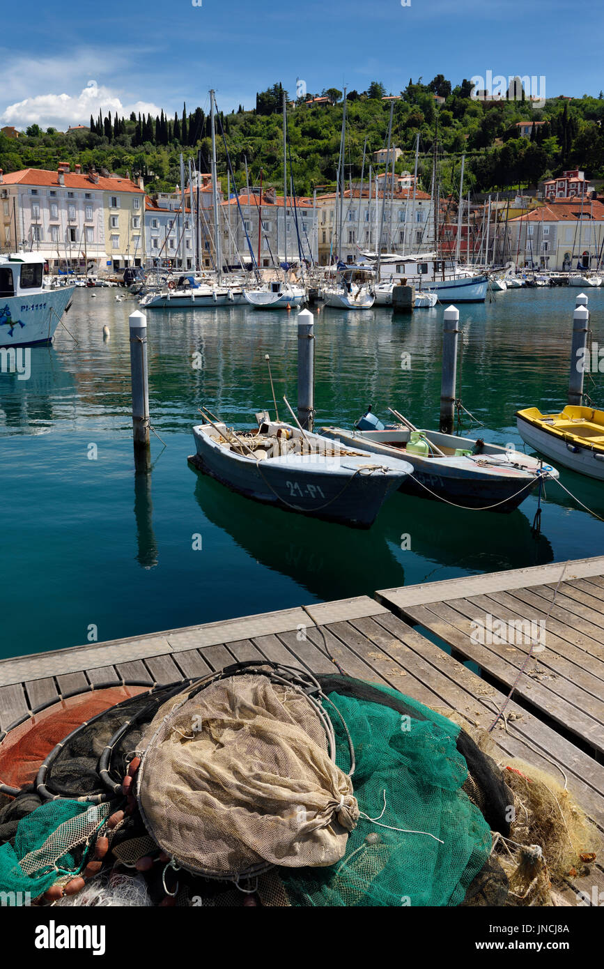 Le reti da pesca sul dock di Pirano in Slovenia con barche e velieri ormeggiati in porto sulla costa sul Mare Adriatico Foto Stock