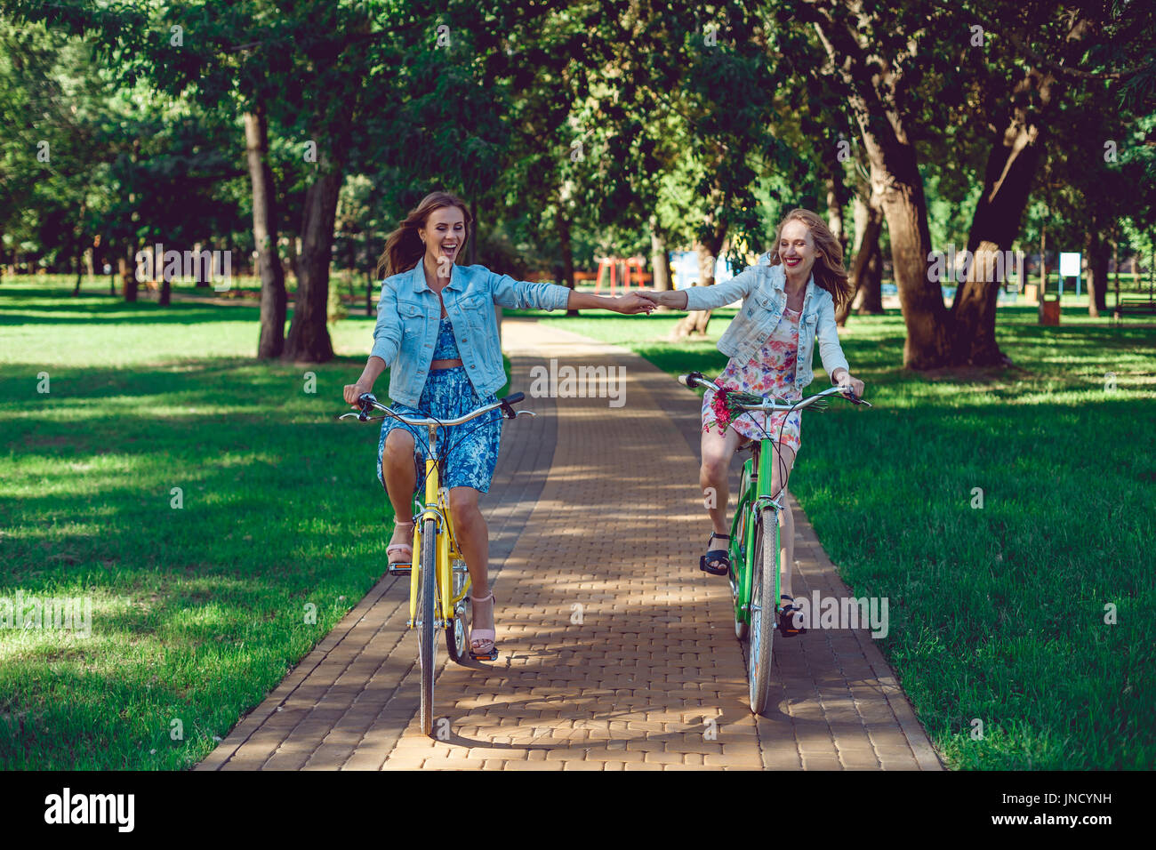 Amici di sesso femminile godendo di escursioni in bicicletta su un giorno di estate, tenendo le mani. Foto Stock