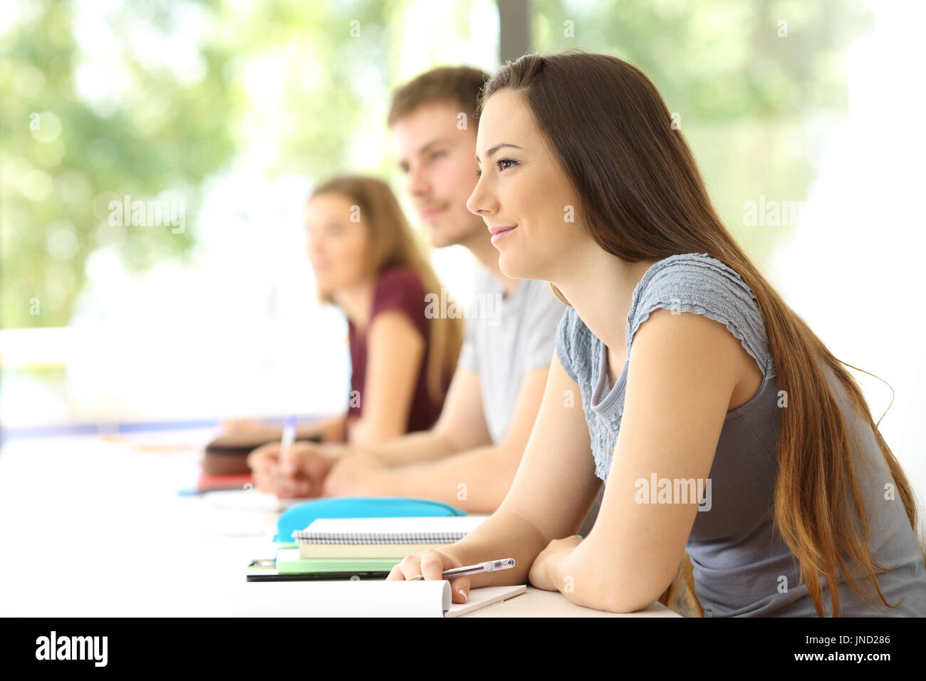 Gli studenti ascolto di una lezione in aula con altri compagni di classe in background Foto Stock