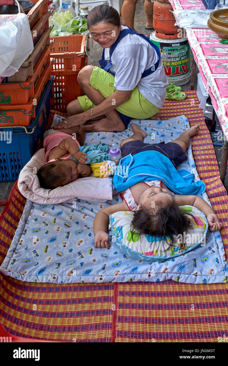 I bambini che dormono per esterno a un Tailandia street sede di mercato. Lavorando la madre e il bambino. Foto Stock