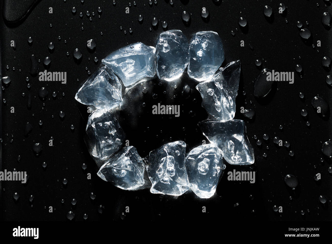 Cubetti di ghiaccio in un cerchio con gocce d'acqua tutto intorno, su un metallo nero lo sfondo di superficie Foto Stock