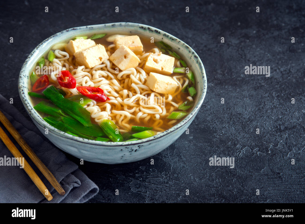 Giapponese zuppa ramen con tofu in pietra scura sullo sfondo. Zuppa di miso con spaghetti ramen e tofu in vaso di ceramica, asiatica del cibo tradizionale. Foto Stock