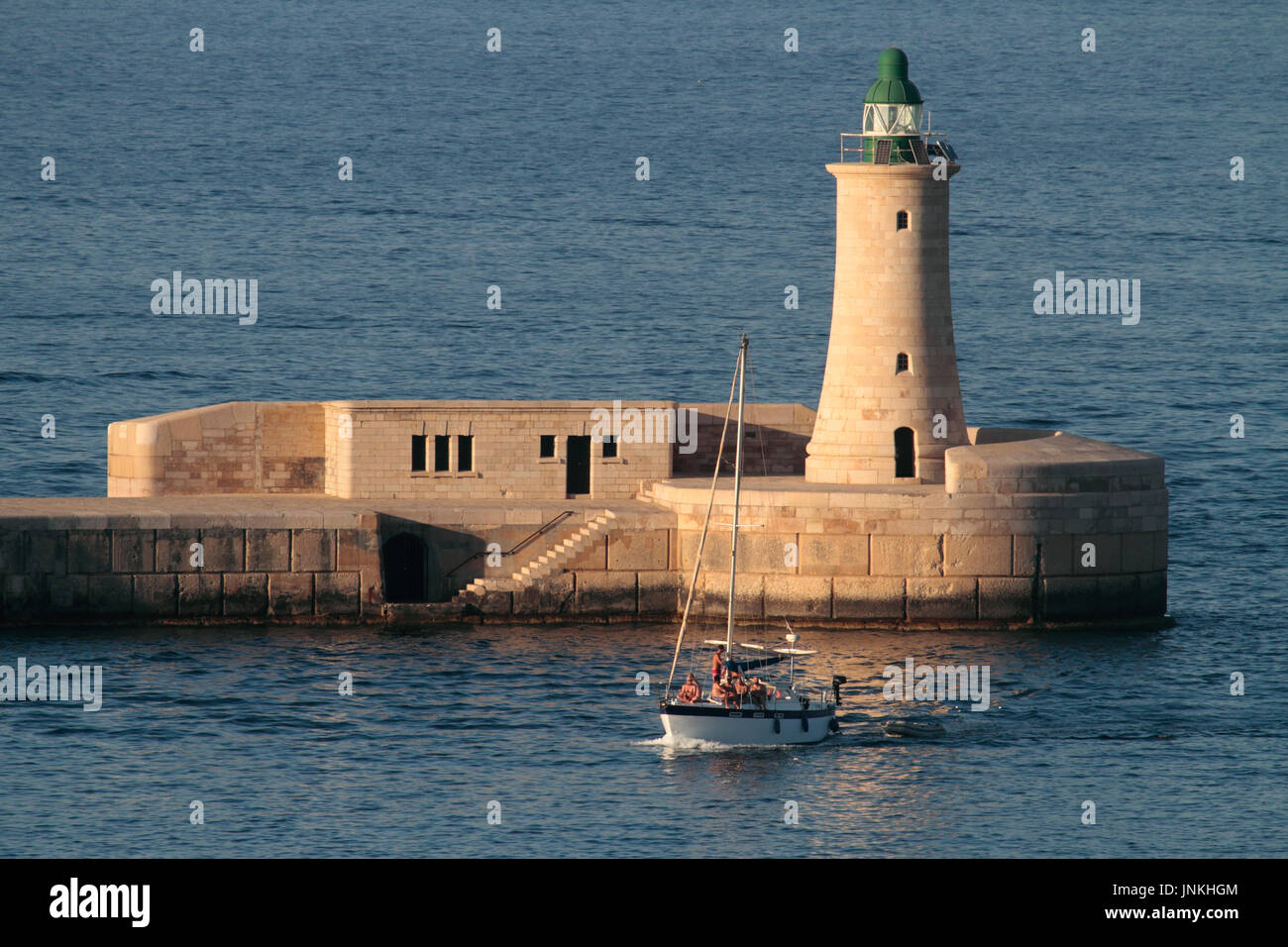 A vela nel Mediterraneo. Yacht passando dal faro di frangiflutti che entra in Malta il Grand Harbour Foto Stock