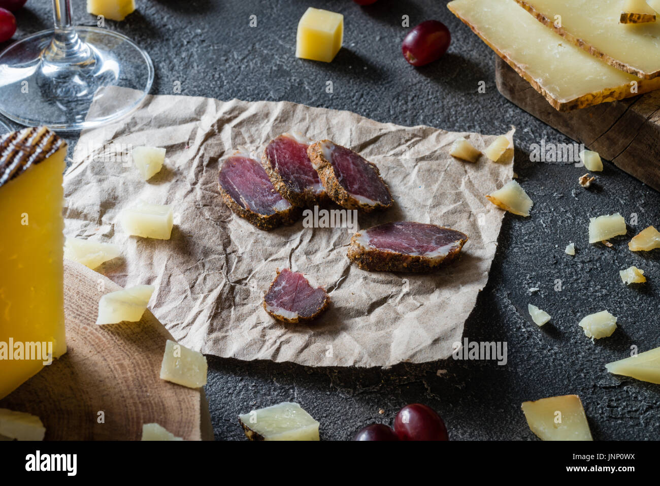 Fette di carne secca tritata spagnolo hard formaggio manchego in legno tagliato a fette, italiano il pecorino toscano, uve rosse scuro su sfondo rustico, picni Foto Stock