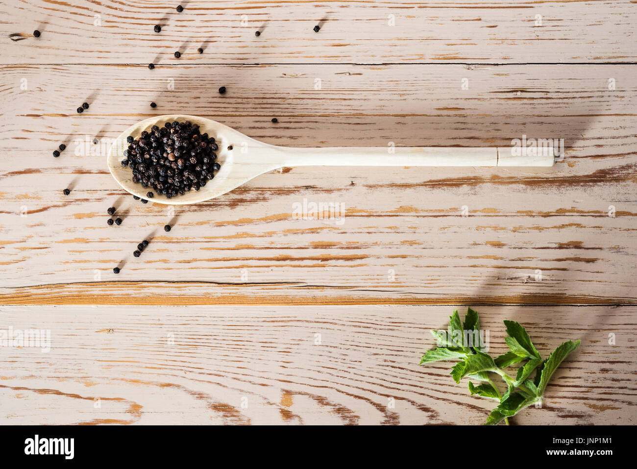 Scatto dall'alto di un cucchiaio di legno su turbati da tavolo, con grani di pepe nero. Foto Stock