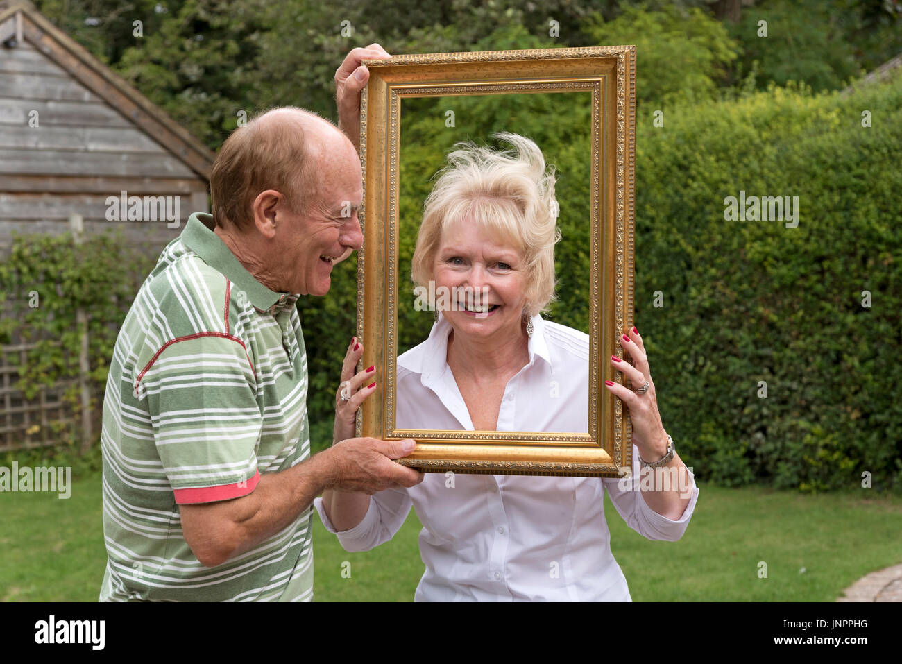 Coppia di anziani a giocare con la cornice di una foto in un ambiente da giardino Foto Stock