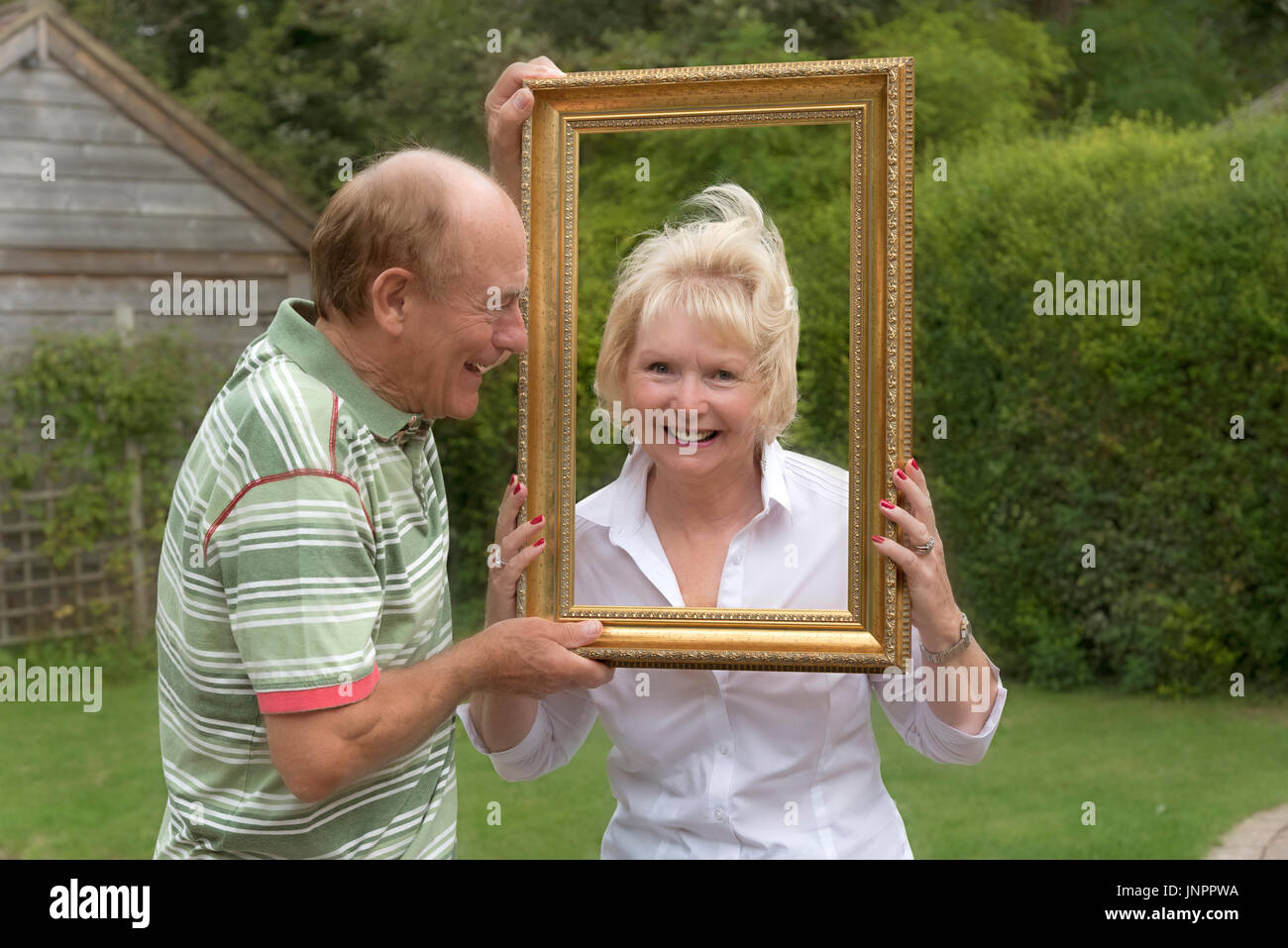 Coppia di anziani a giocare con la cornice di una foto in un ambiente da giardino Foto Stock
