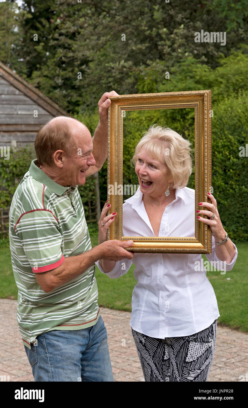 Coppia di anziani a giocare con la cornice di una foto in un ambiente da giardino Foto Stock