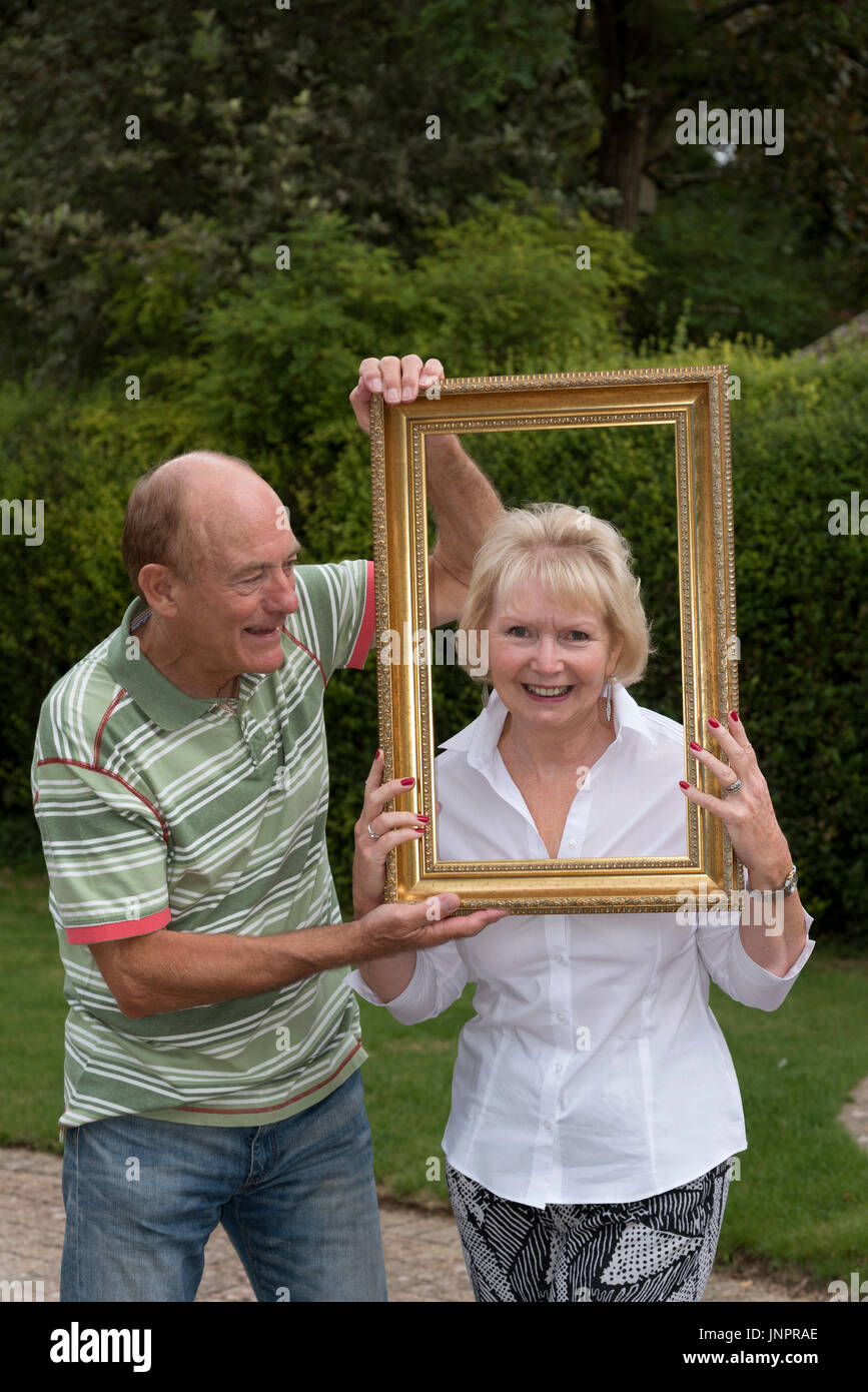 Coppia di anziani a giocare con la cornice di una foto in un ambiente da giardino Foto Stock