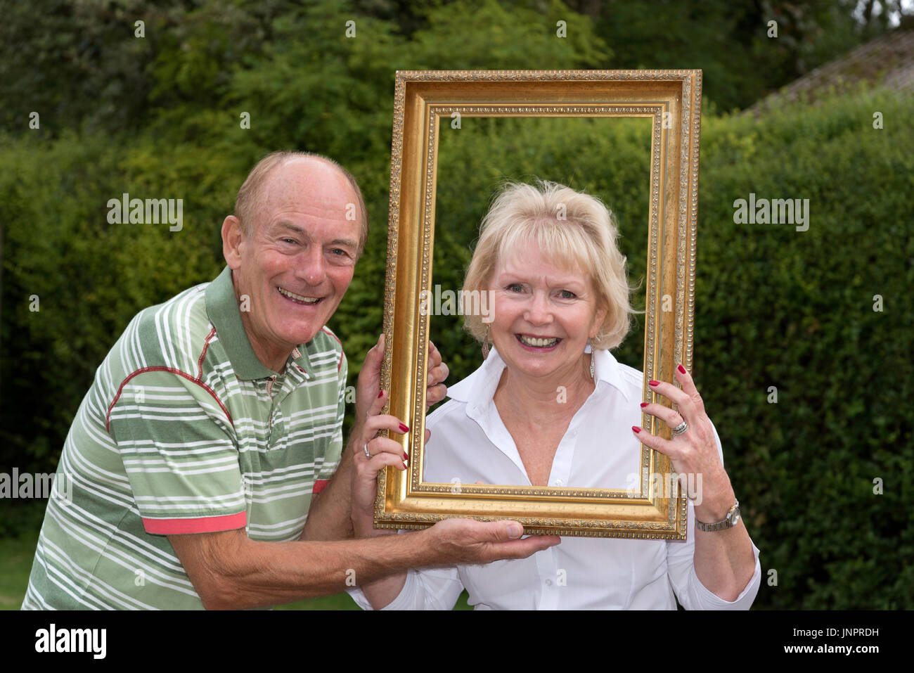 Coppia di anziani a giocare con la cornice di una foto in un ambiente da giardino Foto Stock
