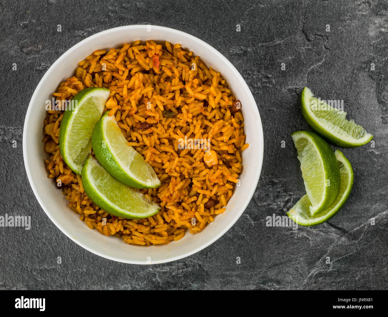 Ciotola di piccante riso messicano con lime fresco contro un nero ardesia Sfondo piastrelle Foto Stock